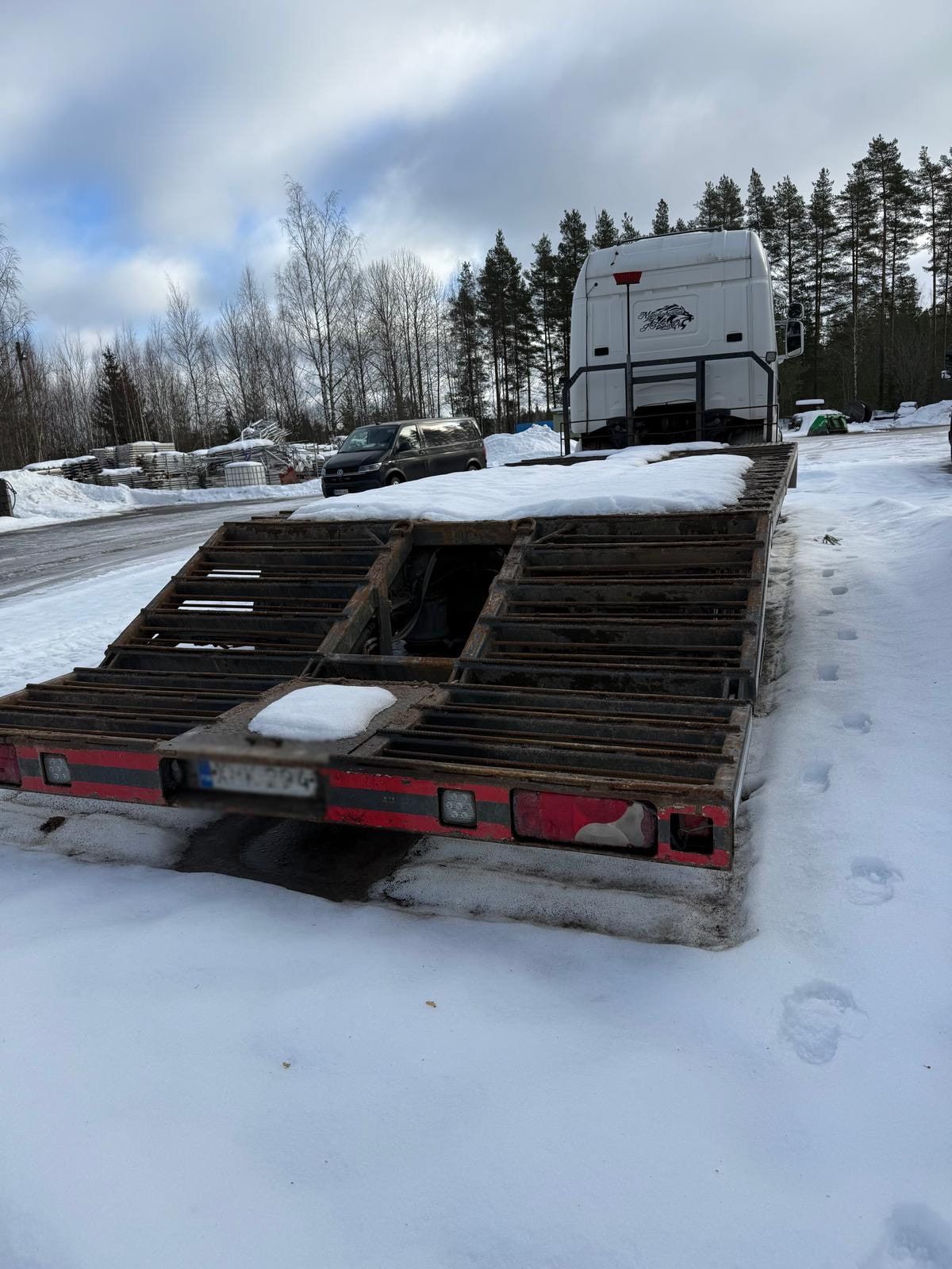 Lumipeitteinen kuljetuslavetti kuorma-auton takana talvisella pihalla.