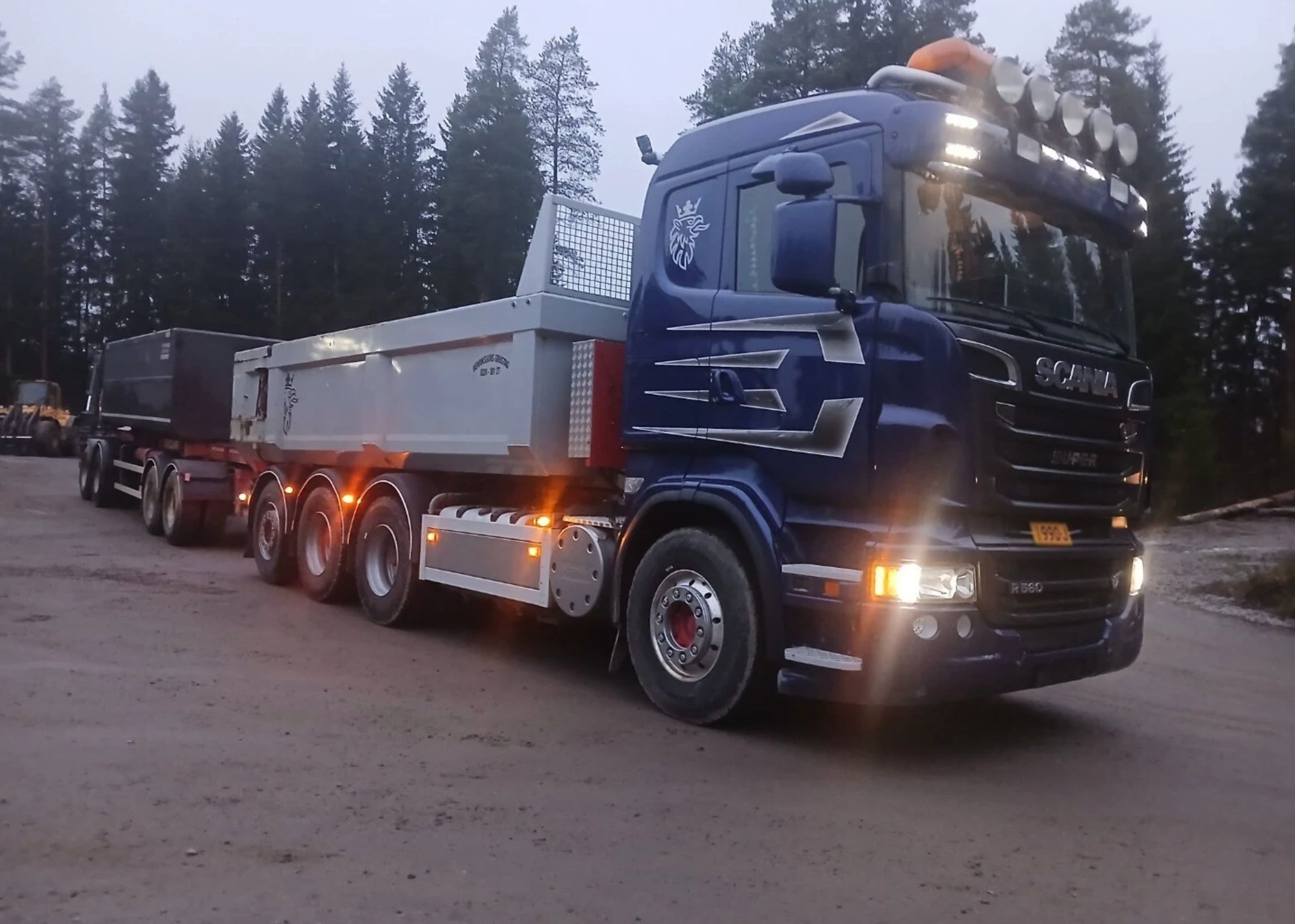 Tummansininen sora-auto metsätiellä.