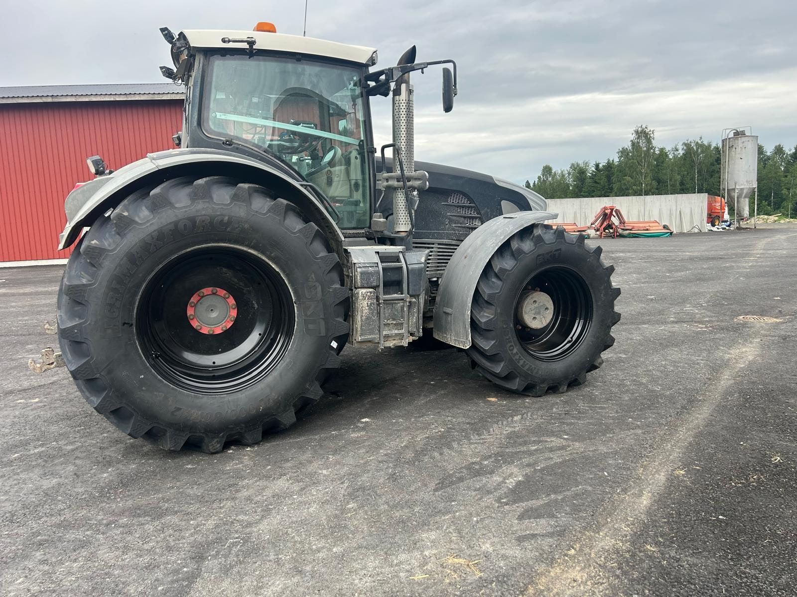 Tumma traktori sorapihalla maatilan rakennusten vieressä.